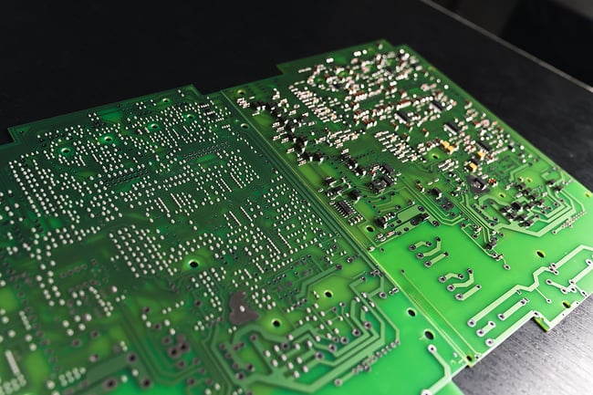 Close up photo of a green printed circuit board laying on a black wooden desk.