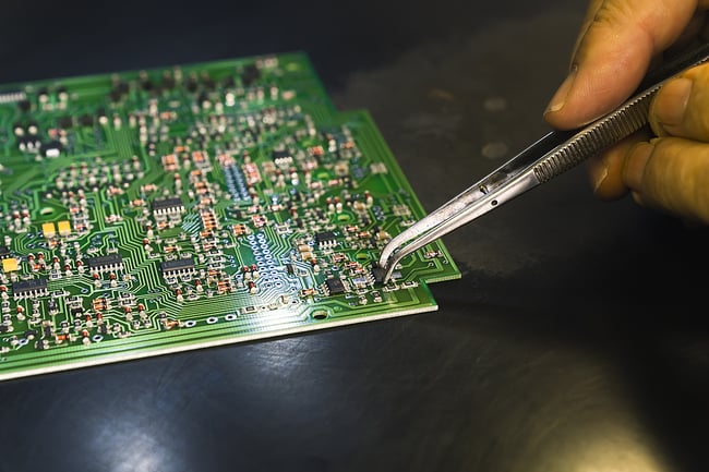 close up photo of a mans hand working on a printed circuit board with curved tweezers