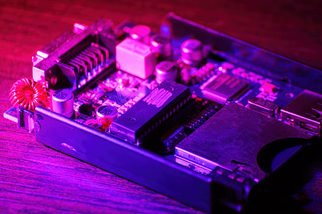 small printed circuit board inside an electronic sitting on a wooden table under blue and red LED lights