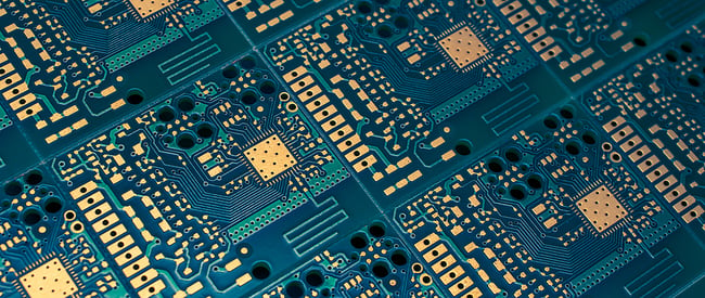 Close up photo of a printed circuit board with a green base and gold components