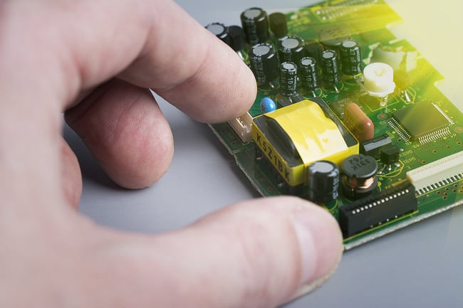 Close up of technician's hand next to a printed circuit board.