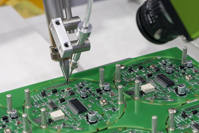 Close up photo of a robotic arm working on a green printed circuit board.