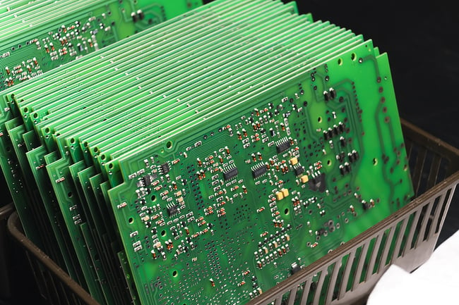 Small brown plastic basket with a stack of green printed circuit boards standing on end.